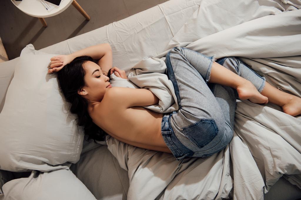 vue du dessus de belle fille asiatique seins nus en jeans dormir sur le lit à la maison
  - Photo, image