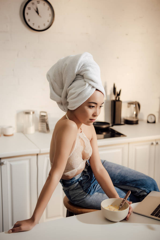 Aziatisch meisje met handdoek gericht op het hoofd met behulp van de laptop tijdens het ontbijt thuis - Foto, afbeelding