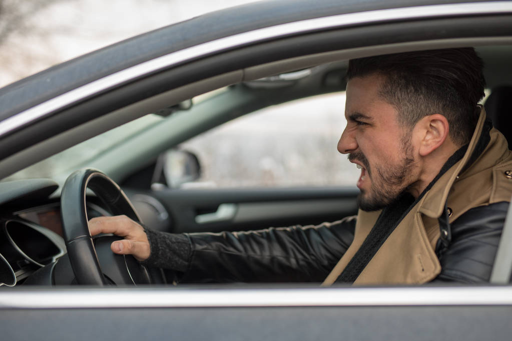 Handsome young man honking in his car while screaming at someone daytime - Photo, Image