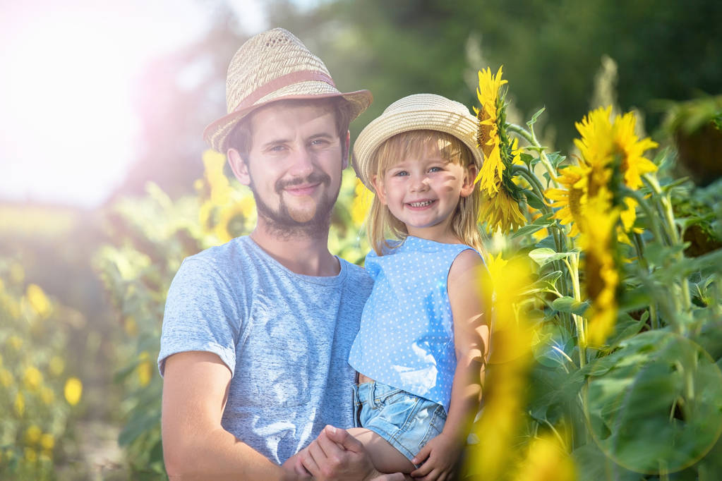 Father and daughter cuddle in the sunflower field. Looking to camera. - Photo, Image