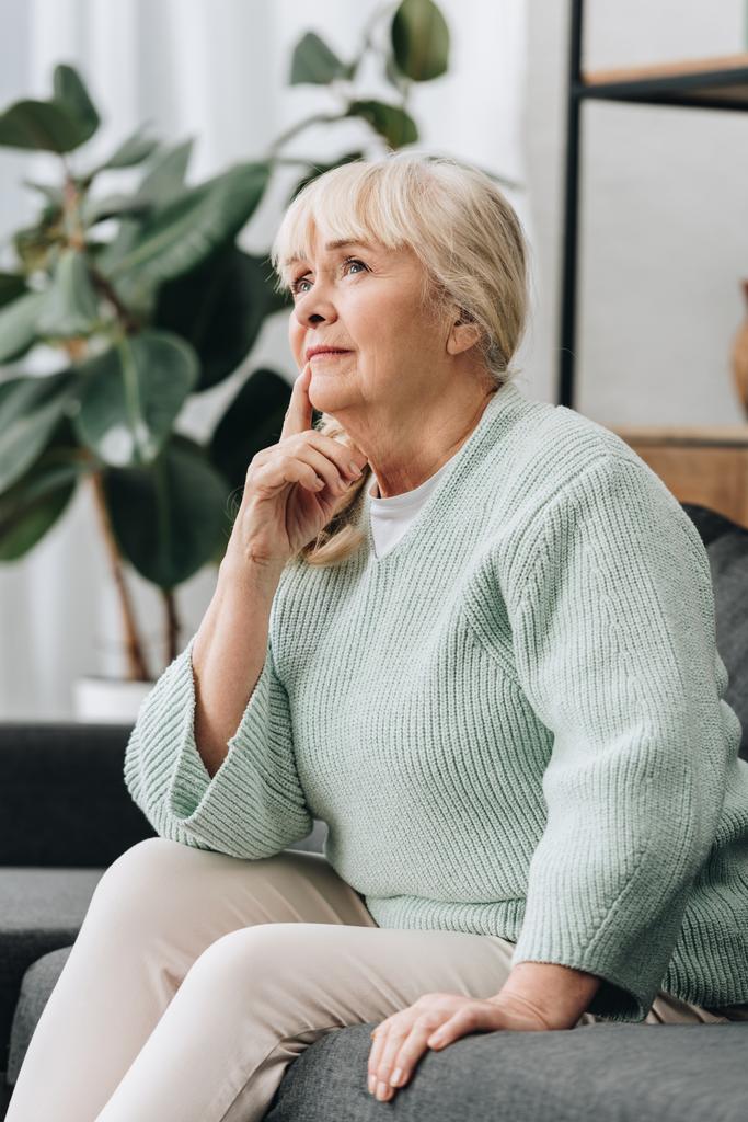 Nachdenkliche Seniorin sitzt auf Sofa im Wohnzimmer  - Foto, Bild