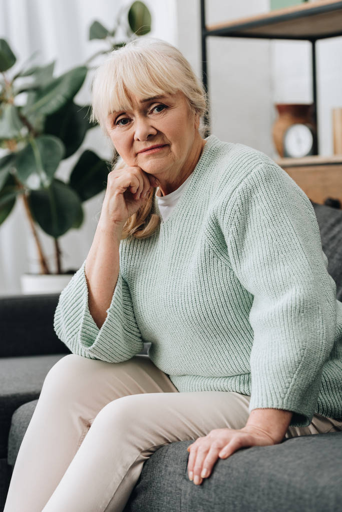 θλιβερή συνταξιούχος γυναίκα με ξανθά μαλλιά που κάθεται στον καναπέ  - Φωτογραφία, εικόνα