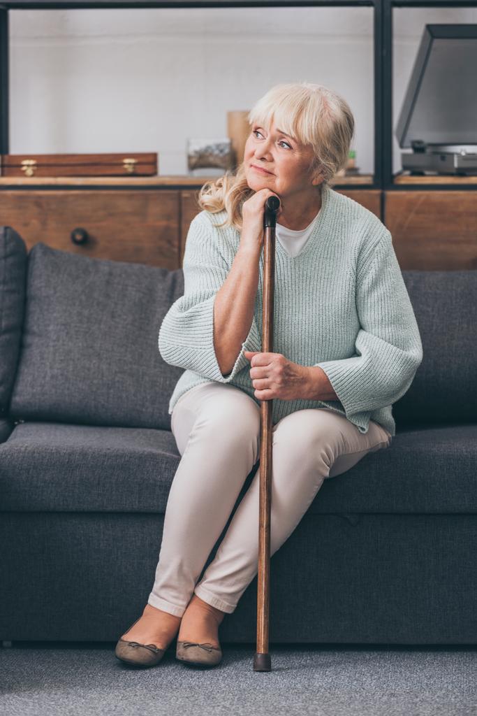 upset senior woman with walking cane sitting on sofa at home - Photo, Image