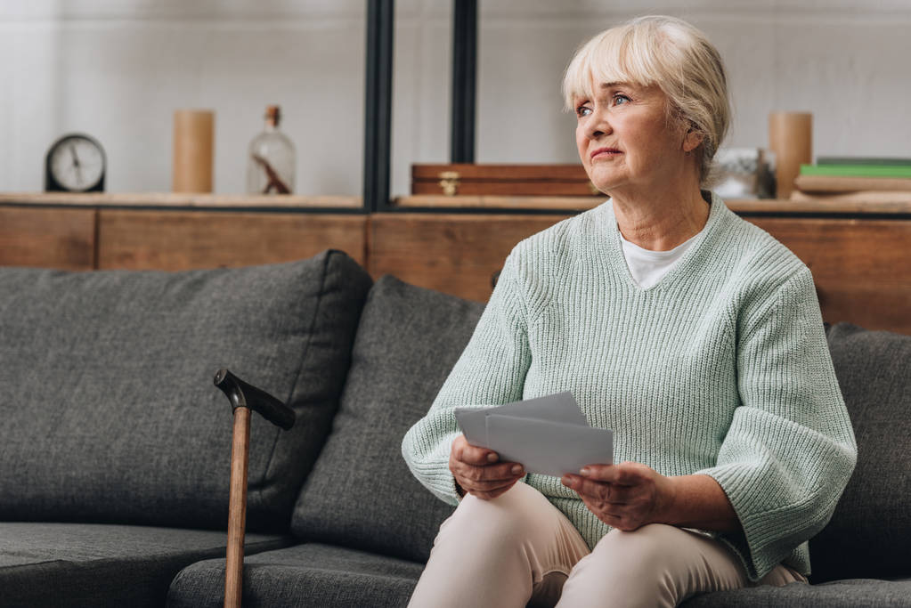 chateado aposentado mulher com cabelo loiro segurando fotos antigas enquanto sentado no sofá
 - Foto, Imagem