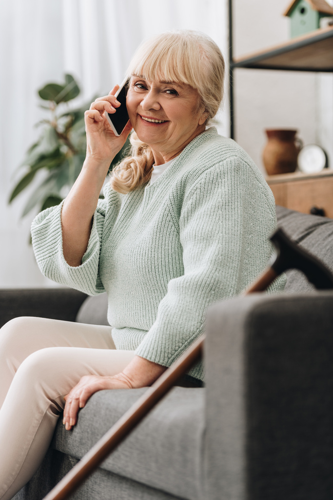 веселая пожилая женщина разговаривает на смартфоне, сидя на диване
 - Фото, изображение