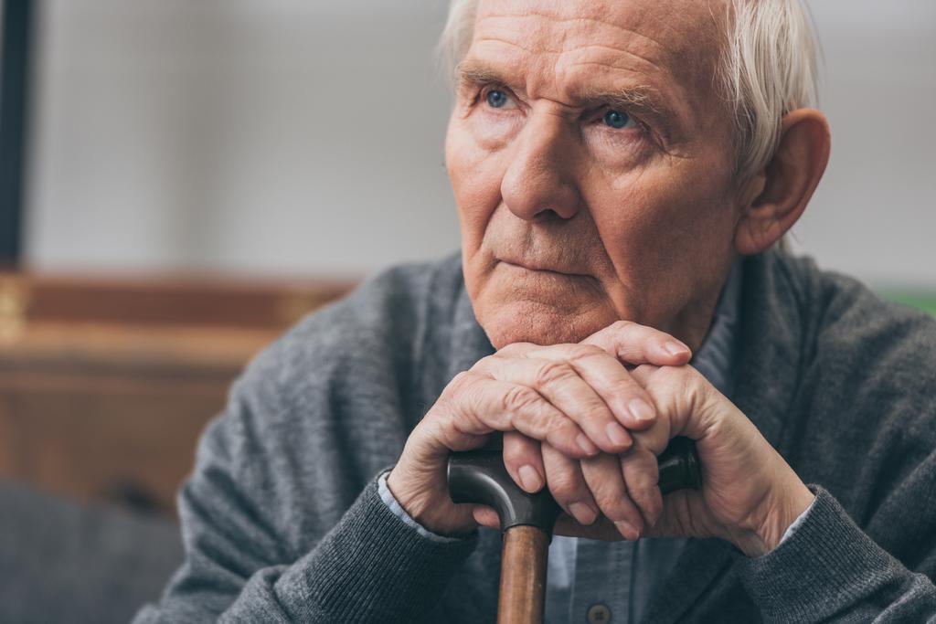 Nahaufnahme eines Rentners mit grauen Haaren, der einen Gehstock hält  - Foto, Bild