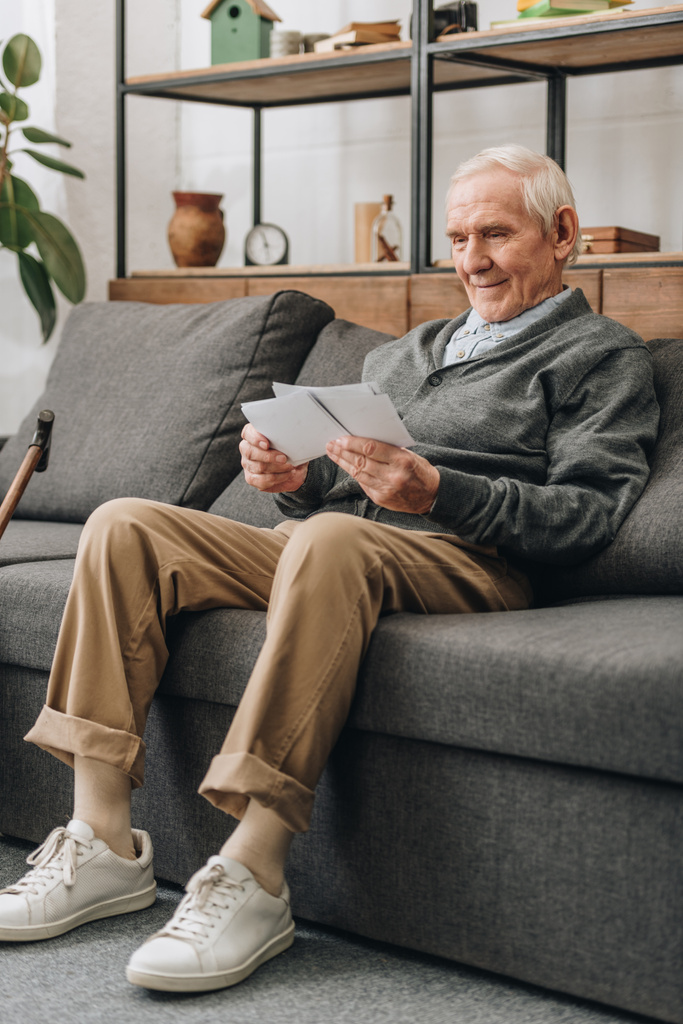 усміхнений пенсіонер з сірим волоссям дивиться на фотографії і сидить на дивані
  - Фото, зображення