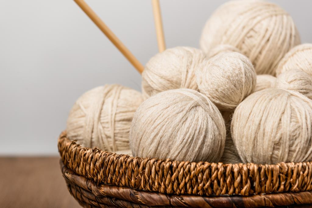 close up view of yarn clews and knitting needles in wicker basket on grey background - Photo, Image