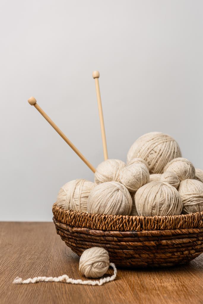 close up view of knitting balls with knitting needles in wicker basket on wooden surface on grey backdrop - Photo, Image