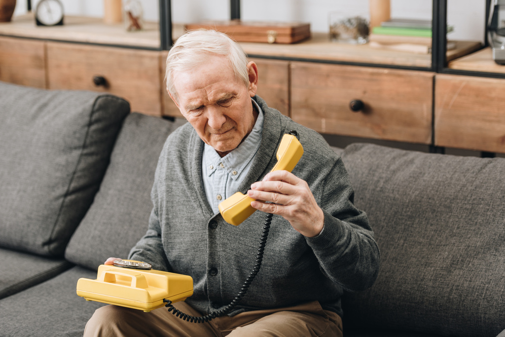 aposentado homem olhando para telefone velho enquanto sentado no sofá
 - Foto, Imagem