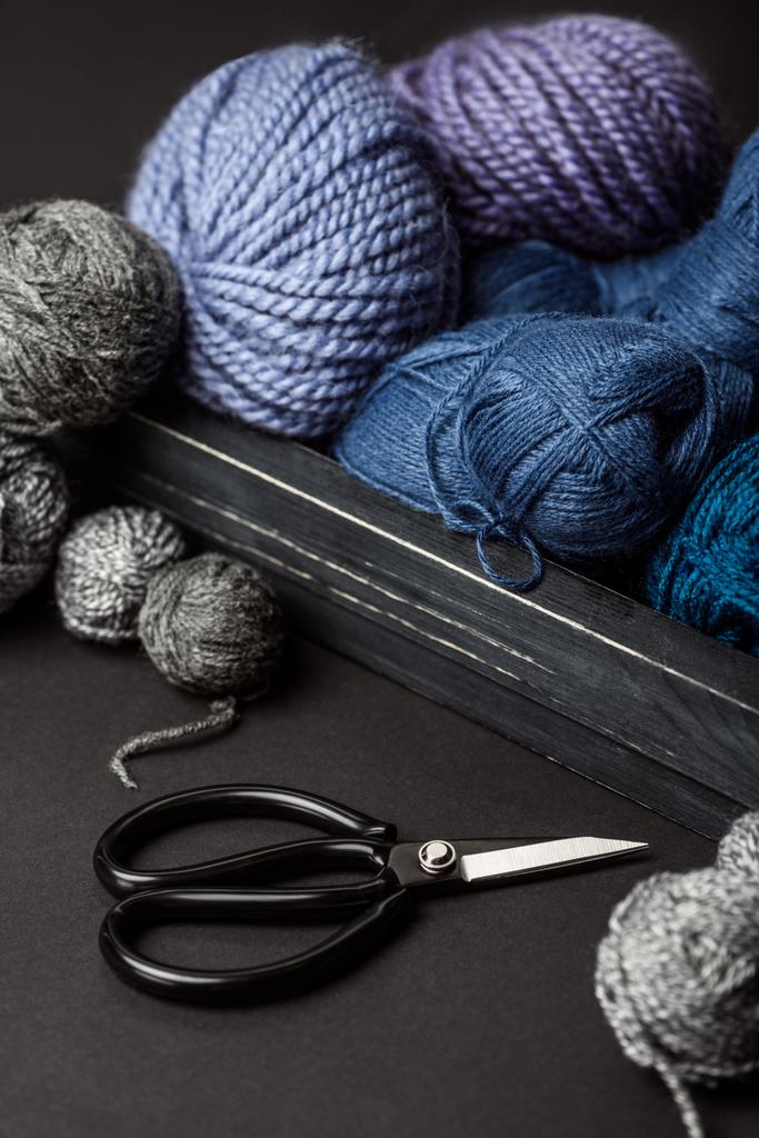 close up view of grey, purple and blue knitting clews in wooden box on grey tabletop with scissors - Photo, Image