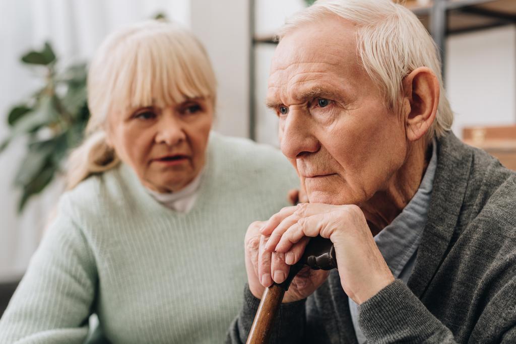 Selektywny fokus smutny emeryt siedzi w pobliżu starszy żona w domu  - Zdjęcie, obraz