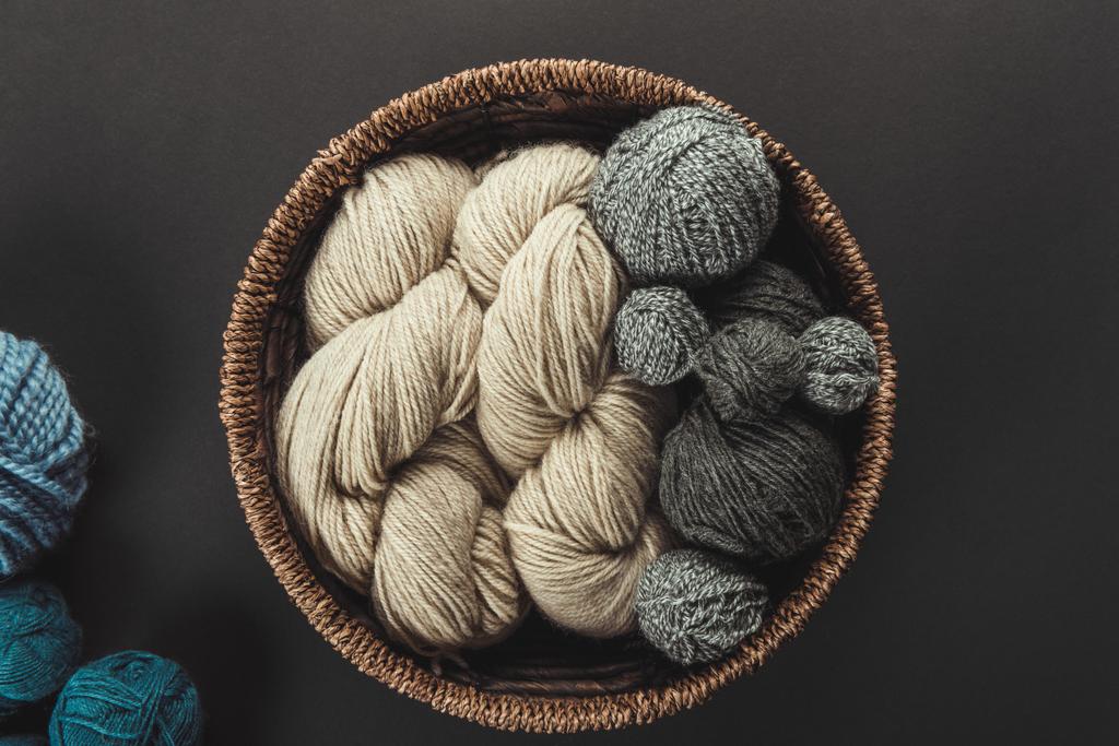 top view of beige and grey knitting clews in wicker basket on grey backdrop with blue yarn - Photo, Image