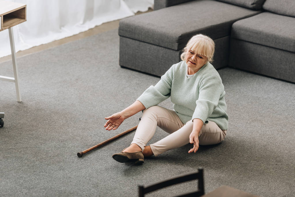безпорадна старша жінка з світлим волоссям, що сидить на підлозі біля дивана
  - Фото, зображення