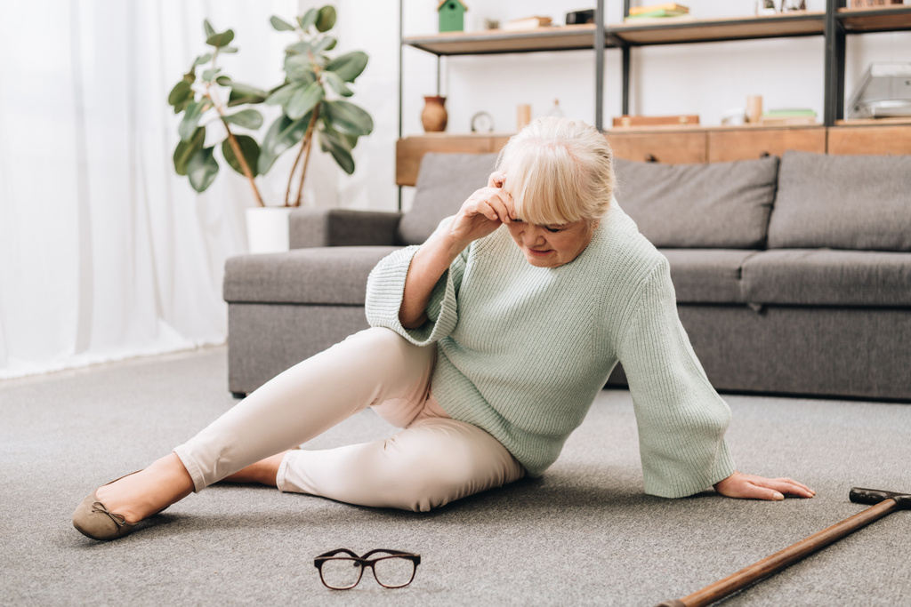 mujer mayor sentada en el suelo en la sala de estar y con dolor de cabeza
  - Foto, Imagen