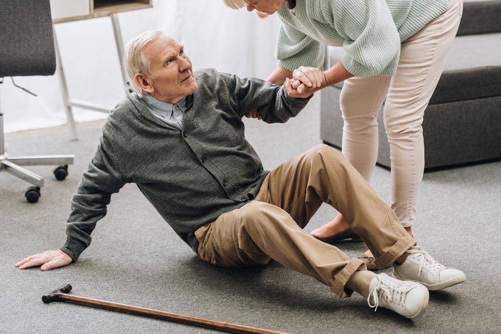 old woman helping to stand up husband who falled down on floor near walking stick - Photo, Image
