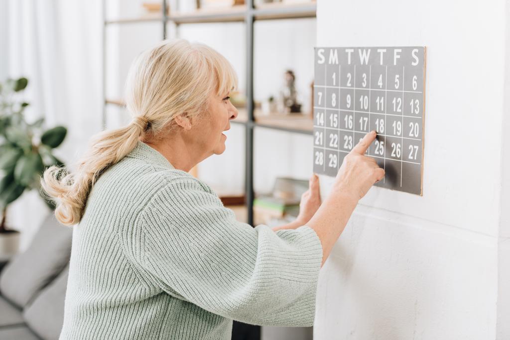Starší žena dotýká Nástěnný kalendář a při pohledu na data - Fotografie, Obrázek