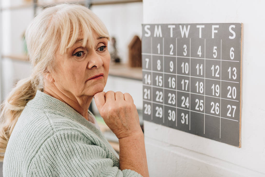 chateado mulher sênior tocando calendário parede e lembrando datas
 - Foto, Imagem