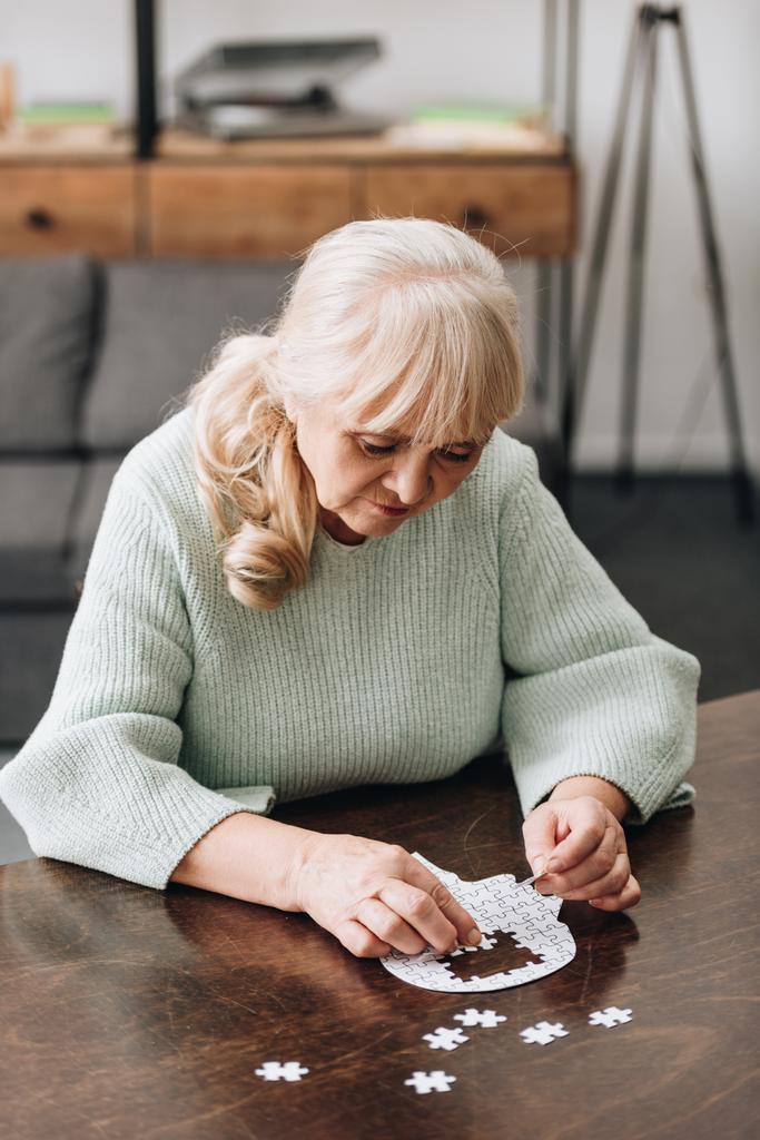 Seniorin mit blonden Haaren spielt mit Puzzles auf Tisch - Foto, Bild