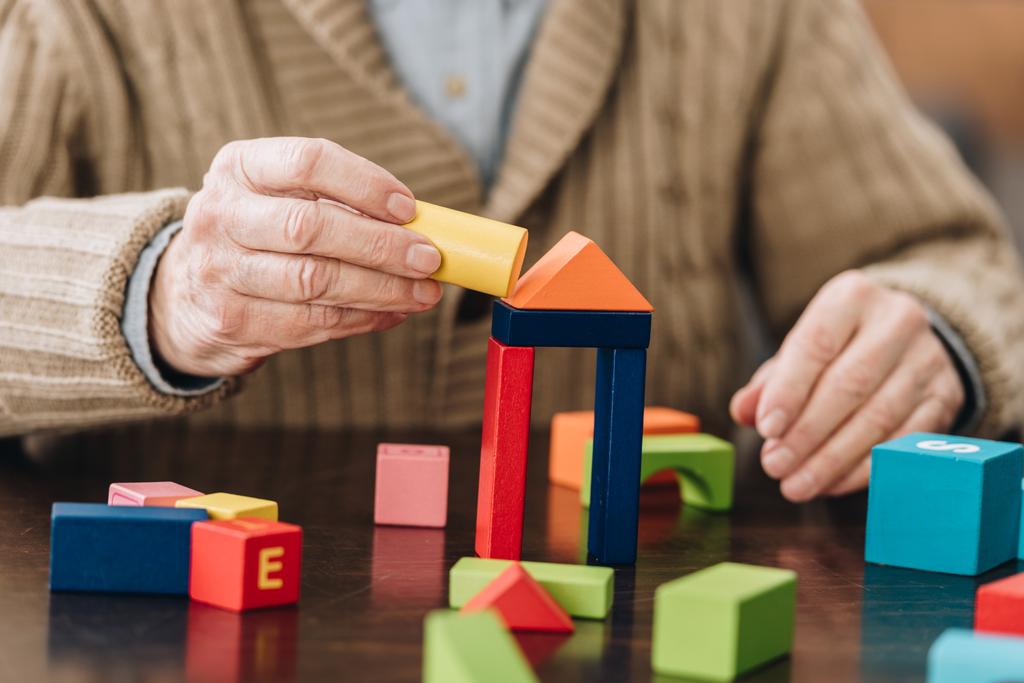 обрезанный вид пожилого человека, играющего с деревянными игрушками на столе
 - Фото, изображение