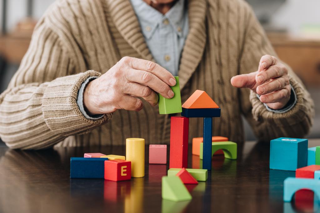 Ausgeschnittener Blick auf Senior, der zu Hause mit Holzspielzeug spielt - Foto, Bild