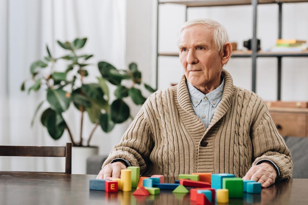 Senior man zit in de buurt van houten speelgoed thuis - Foto, afbeelding