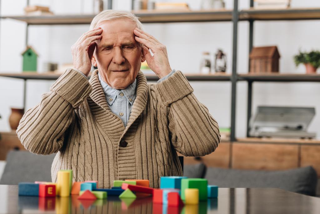 pensionista com dor de cabeça enquanto sentado perto de brinquedos de madeira
  - Foto, Imagem