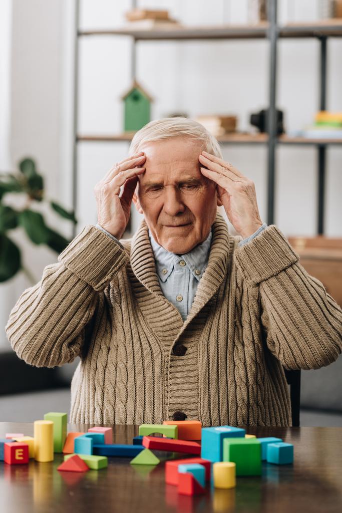 pensionista tendo dor de cabeça enquanto sentado perto de brinquedos de madeira em casa
  - Foto, Imagem