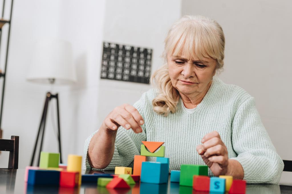 blonde gepensioneerde vrouw spelen met houten speelgoed thuis - Foto, afbeelding