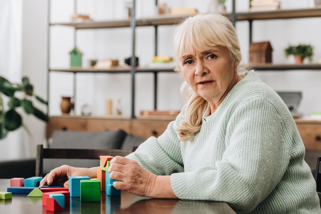 blond kobieta senior siedzący w pobliżu drewniane zabawki w domu - Zdjęcie, obraz