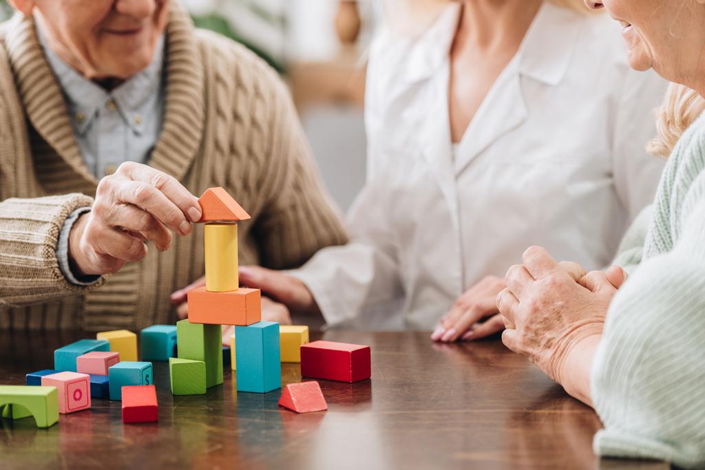 cropped view of caregiver sitting with retired man and woman and playing with wooden toys  - Photo, Image