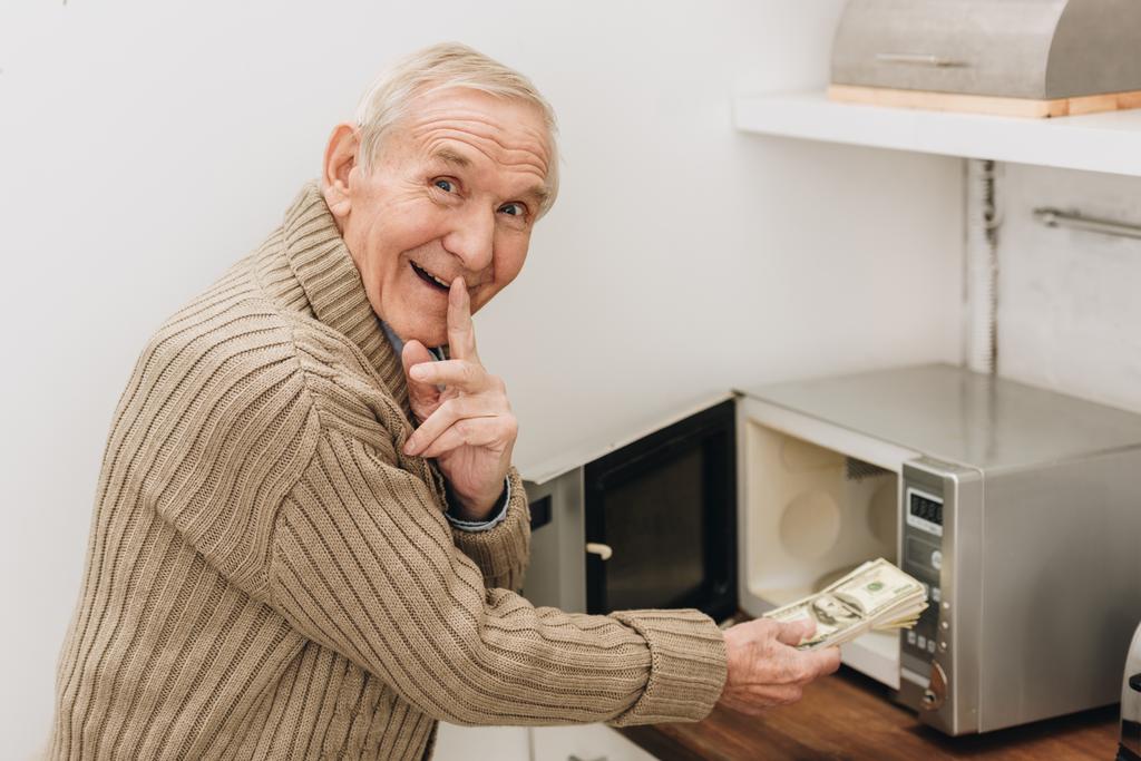 iloinen vanhempi mies asettamalla sormi huulille sanoa hiljaa samalla rahaa mikroaaltouunissa
  - Valokuva, kuva