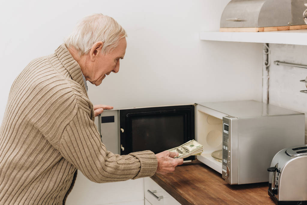 Ανώτερος άνθρωπος με άνοια νόσου βάζοντας δολάρια σε φούρνο μικροκυμάτων  - Φωτογραφία, εικόνα