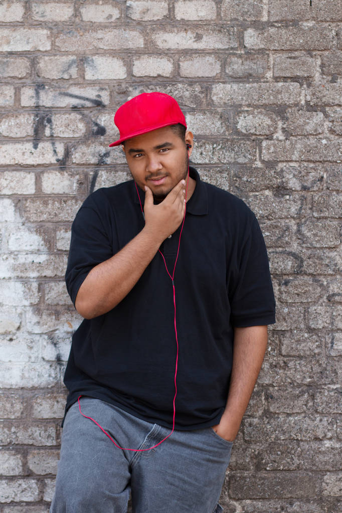 Jeune homme noir posant au mur de briques grises sur son bloc
 - Photo, image