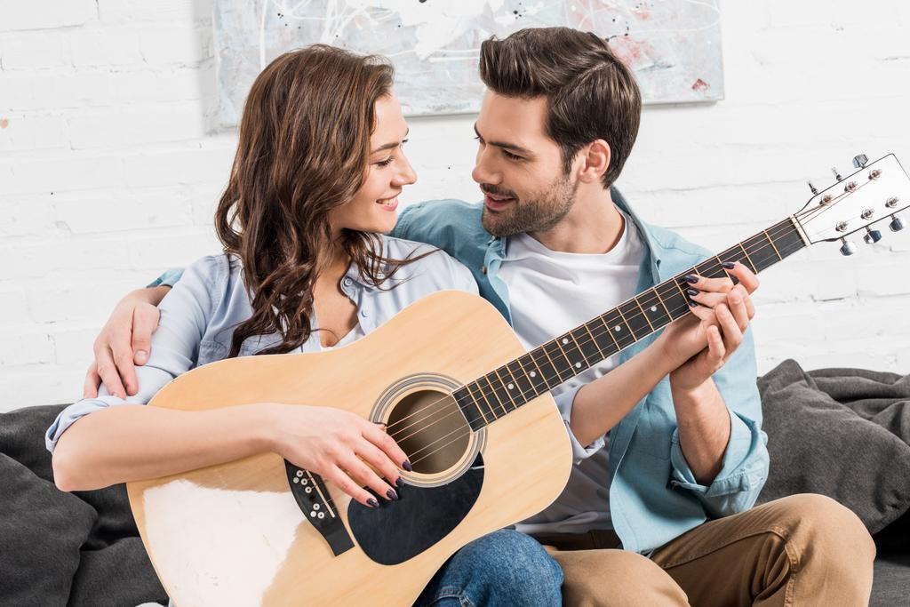 pareja sentada en el sofá y tocando la guitarra acústica en casa
 - Foto, Imagen