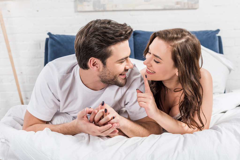 ζευγάρι ξαπλωμένο στο κρεβάτι ενώ γυναίκα χαμογελώντας και δείχνοντας με το δάχτυλο - Φωτογραφία, εικόνα