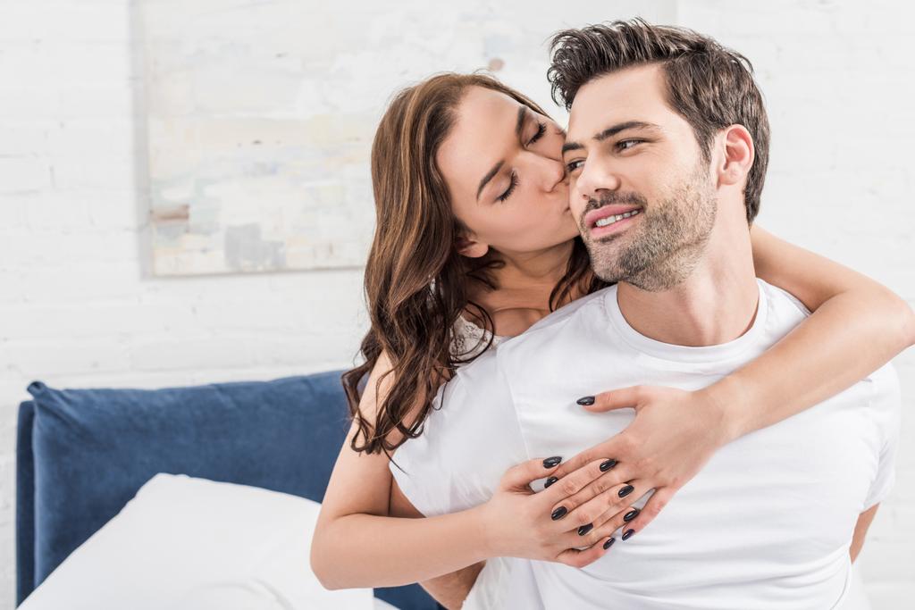 vrouw teder te omhelzen en kussen knappe man in bed - Foto, afbeelding