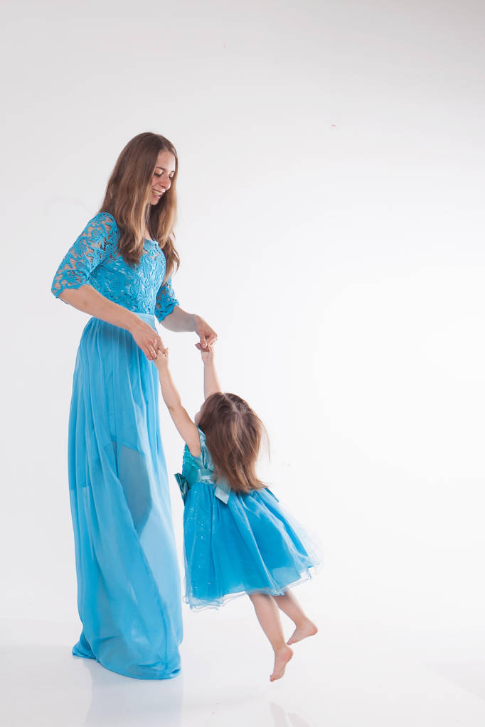 matka i dziecko pozowanie na białym tle. Kobieta i dziewczynka w niebieskim stroju grać - Zdjęcie, obraz