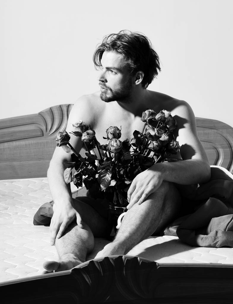 mladý pohledný vousatých sexy macho muž s stylové vousy sedí nahá na posteli pod červenou deku s oranžovou růží v transparentní vas - Fotografie, Obrázek