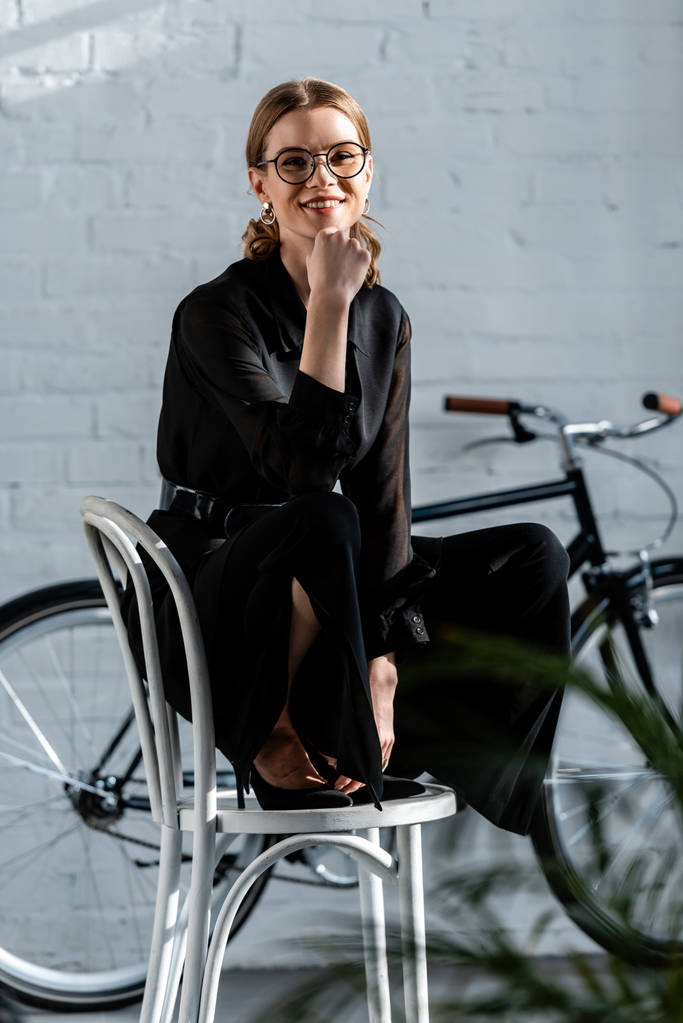 aantrekkelijke vrouw zittend op een stoel en glimlachend op camera - Foto, afbeelding