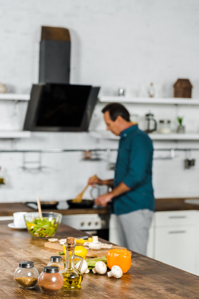 selectieve aandacht van volwassen man frituren groenten in de keuken, kruiden op tafelblad - Foto, afbeelding