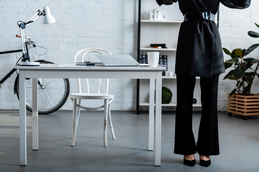 vue recadrée de femme d'affaires en vêtements noirs debout près de la table et de la chaise
 - Photo, image