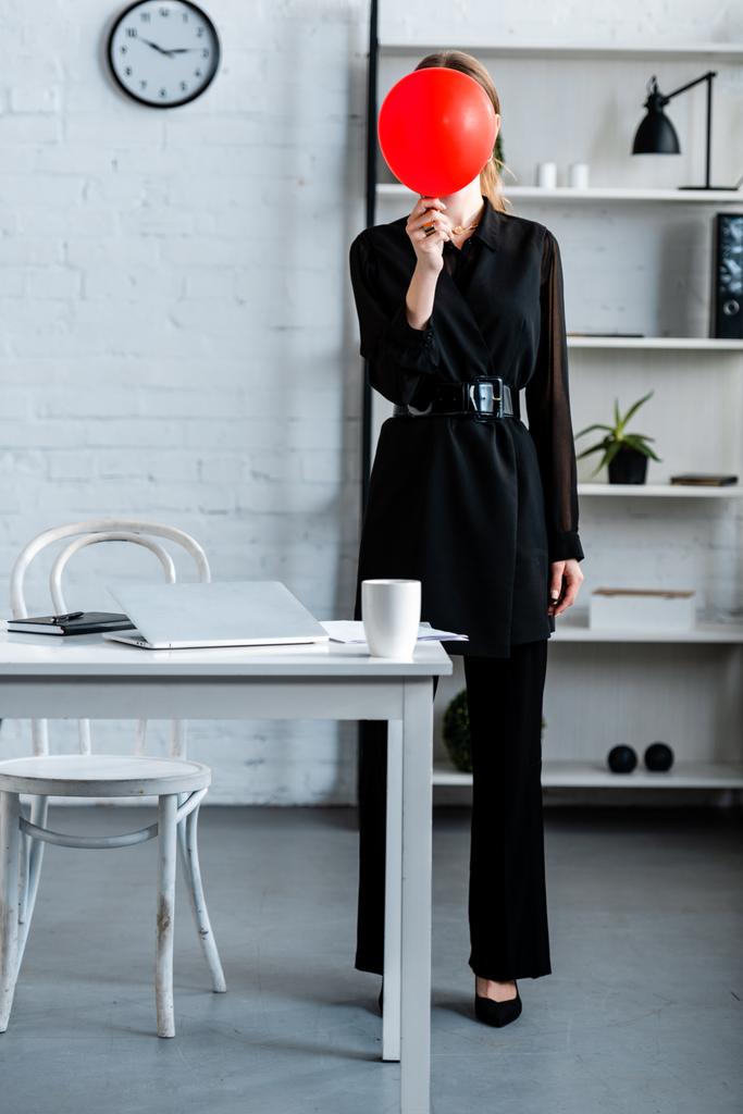 zakenvrouw in zwarte kleding verbergen gezicht achter de rode ballon - Foto, afbeelding