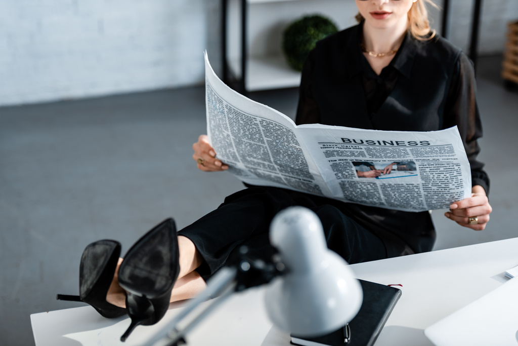 vista ritagliata di donna d'affari in abiti neri seduto a tavola e la lettura di giornale
 - Foto, immagini