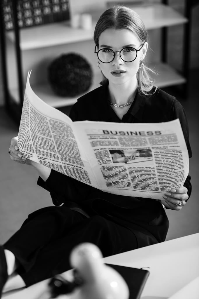 fekete-fehér, a fekete ruhát és cipőt asztalnál ül, és a gazdaság újság szép üzletasszony  - Fotó, kép