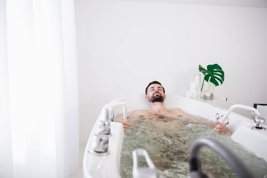 Мирный бородатый мужчина наслаждается сидя в гидромассажной ванне
 - Фото, изображение