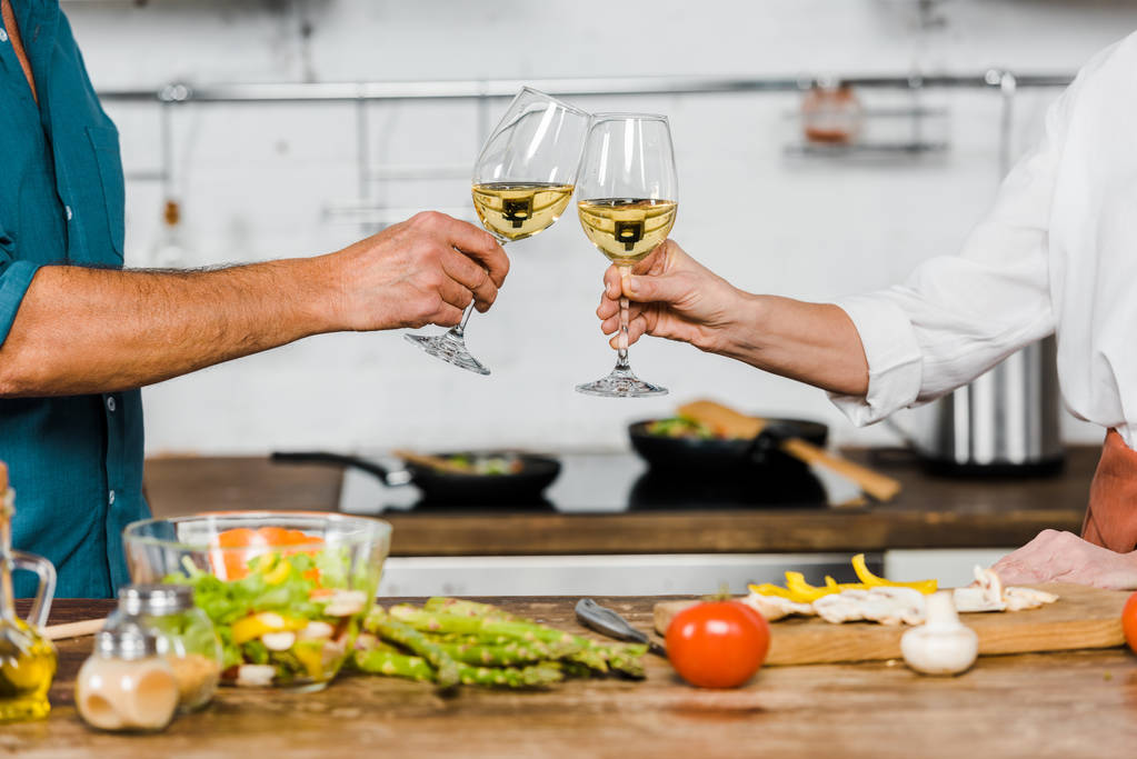 cropped image of wife and husband clinking with glasses of wine in kitchen - Photo, Image
