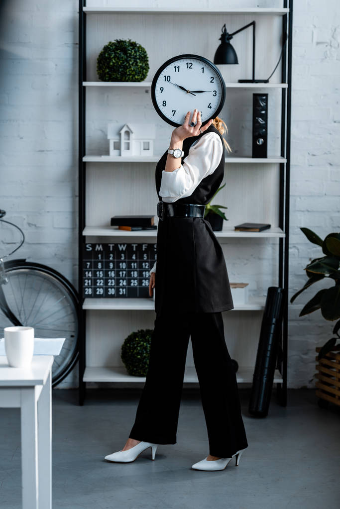 femme d'affaires en tenue de cérémonie horloge devant le visage sur le lieu de travail
 - Photo, image