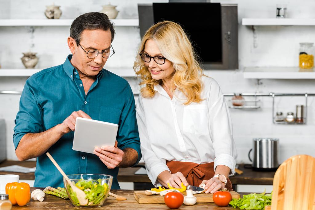 mature husband showing something on tablet to wife in kitchen - Photo, Image