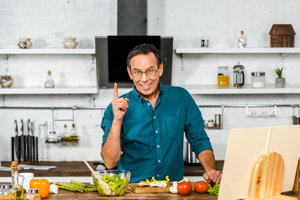 sorridente bell'uomo maturo che cucina in cucina e mostra un dito in su
 - Foto, immagini